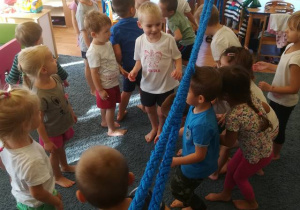 Dzieci przechodzą pod niebieską liną trzymaną przez nauczycielkę